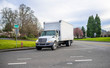 © vit - Small compact semi truck with cube box trailer transporting commercial cargo driving on the street of urban city in spring time with blooming trees