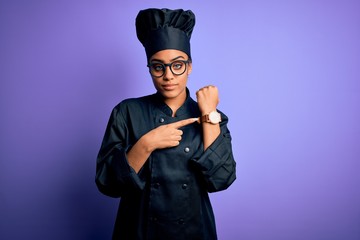 Poster - Young african american chef girl wearing cooker uniform and hat over purple background In hurry pointing to watch time, impatience, looking at the camera with relaxed expression