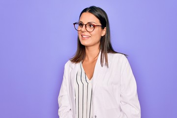 young beautiful brunette psychologist woman wearing coat and glasses over purple background looking 