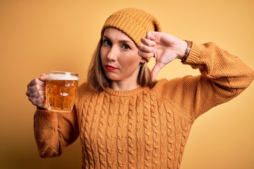 Poster - Young beautiful blonde woman drinking jar of beer standing over isolated yellow background with angry face, negative sign showing dislike with thumbs down, rejection concept