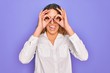 © Krakenimages.com - Young beautiful woman with blue eyes wearing casual shirt and glasses over purple background doing ok gesture like binoculars sticking tongue out, eyes looking through fingers. Crazy expression.