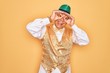 © Krakenimages.com - Middle age senior grey-haired man wearing Brazilian carnival custome over yellow background doing ok gesture like binoculars sticking tongue out, eyes looking through fingers. Crazy expression.