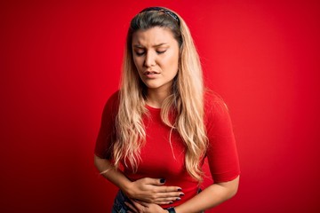 Canvas Print - Young beautiful blonde woman wearing casual t-shirt standing over isolated red background with hand on stomach because indigestion, painful illness feeling unwell. Ache concept.