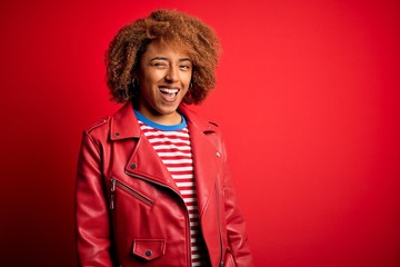 Wall Mural - Young beautiful African American afro woman with curly hair wearing casual red jacket winking looking at the camera with sexy expression, cheerful and happy face.