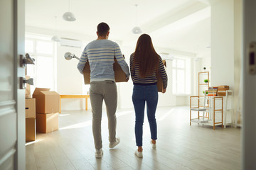 Rear view moving. Young couple family with boxes to move in a new house room.