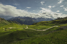 Panorama From Grossglockner Pass At Hochtor On A Summer Day With Beautiful Clouds, Green Meadows And Winding Road Seen Below. Summer On Mountain Pass.