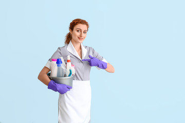 Wall Mural - Beautiful young chambermaid with cleaning supplies on color background