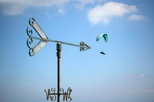 Arrow Shape Weathervane Against Summer's Sky With Cumulus And Paragliders In Background, Italian Alps. Italy