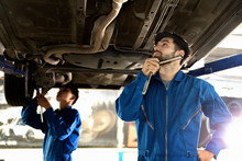 Mechanic Using Screwdriver For Repair With Repair Equipment Standing Under The Car In Maintainance Service Center Which Is A Part Of Showroom.Car Maintenance And Repair Concept.