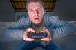 © TheVisualsYouNeed - indoors portrait of young excited and concentrated man at home playing videogames holding controller looking stressed and focused in video gaming addiction