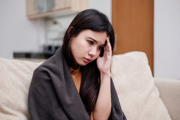 Wall Mural - Portrait of Young woman sitting on a couch, holding her head, having a strong headache. Pandemic 2019 Coronavirus 2019-nCoV Concept.