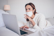 © Алина Троева - Young european woman in face medicine mask working on a laptop in bedroom during coronavirus isolation home quarantine. Covid-19 pandemic Corona virus. Distance online work from home concept.
