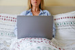 Close up shot of young blonde woman working remotely at home due to coronavirus quarantine concept. Beautiful female sitting in bed with laptop. Background, copy space.
