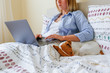 Close up shot of young woman working remotely from home in her bed on laptop due to coronavirus quarantine. Freelancer female with her jack russell terrier puppy. Copy space, background,