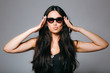 © ChesterAlive91 - Beautiful young brunette woman in sunglasses making kissing expression on grey background.