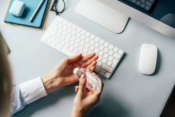 A person treats hands with a disinfector over a working office desk. Self-isolation and hygiene in the epidemic of coronavirus. Stay at home in quarantine and work remotely from home.