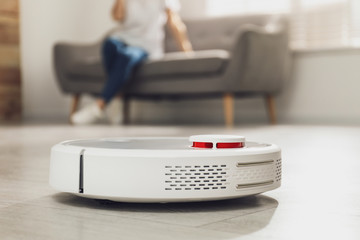 Canvas Print - Woman resting while robotic vacuum cleaner doing her work at home