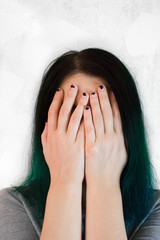 A portrait of unrecognizable young woman with green hair and her hands cover her face