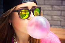 Young Woman In Sunglasses And A Cap Makes A Chewing Gum Bubble