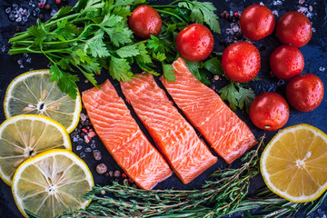 Three salmon steakes with greenery, lemon and cherry tomatoes on the black board