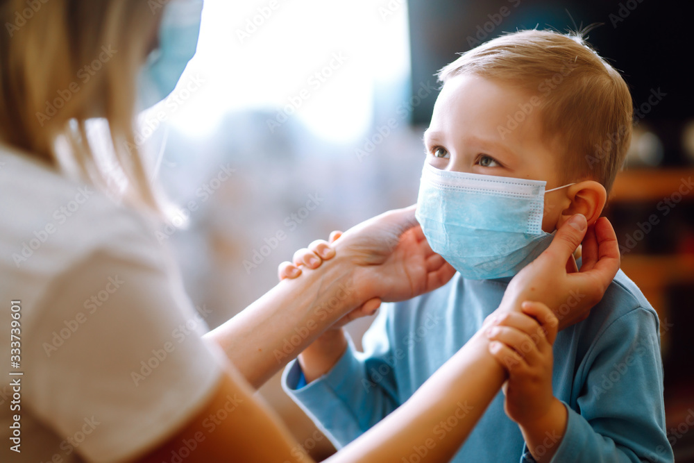 Little boy and mom in medical mask. Mother puts on her baby sterile medical mask. Child, wearing face mask, protect from infection of virus, pandemic, outbreak and epidemic of disease on quarantine. - obrazy, fototapety, plakaty 