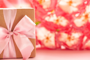 Wall Mural - Gift box wrapped with craft paper and pink bow on pink flowers background.