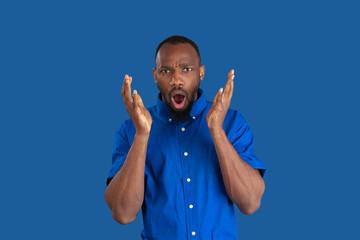 Shocked, astonished. Monochrome portrait of young african-american man isolated on blue studio background. Beautiful male model. Human emotions, facial expression, sales, ad concept. Youth culture.