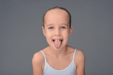 Cheerful white girl shows tongue on a gray background.