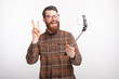 © Vulp - Cheerful young bearded man is making a photo with selfie stick n white background.