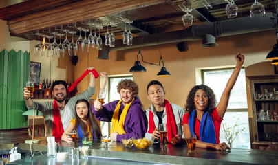 Wall Mural - Sport fans cheering at bar, pub and drinking beer while championship, competition is going. Multiethnic group of friends excited watching translation. Human emotions, expression, supporting concept.