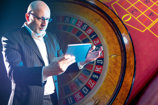 an astonished man with a tablet in his hands on the background of a roulette wheel. losing in an onl