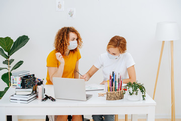 Two redhead girls sitting at the same table in medical masks, working on the picture