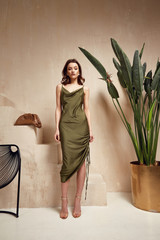 Wall Mural - Fashion model brunette hair wear green silk dress sandals high heels accessory bag clothes for date party walk interior  Sahara journey summer collection plant flowerpot wall stairs beautiful woman.