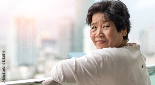 Self quarantine in senior concept. Asia old woman standing at balcony stay at home in urban city to protect from pandamic COVID-19 or novel coronavirus.