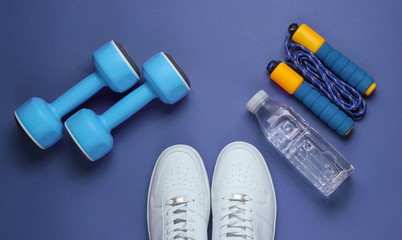 Flat lay style sport concept. Dumbbells, sneakers, jump rope, bottle of water. Sports equipment on purple background. Top view