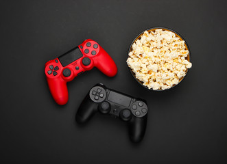 Two gamepads and a bowl of popcorn on black background. Gaming, leisure and entertainment concept. Top view