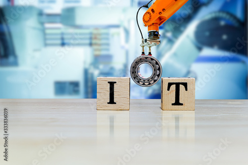 IoT (Internet of Things), Industrial griping robot picking metal part for  build message on wooden desk and machine blue tone color blurred  background, informative about industry 4.0 and IoT concept Stock Photo