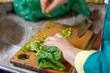 A woman is cutting spinach on a kitchen board.Woman hand cutting spinach using a sharped big kitchen knife on a wooden cutting table surface with more raw fresh leaves ready to be cut. Kitchen actions
