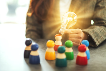 Wall Mural - closeup image of a woman holding and putting a light bulb over one of a different colors wooden peop