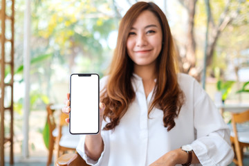 Mockup image of a beautiful asian woman holding and showing black mobile phone with blank white screen