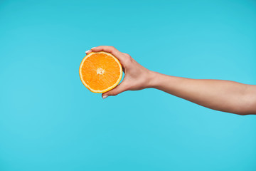 Studio photo of elegant pretty hand keeping half of fresh orange while posing against blue background, going to make fresh juice for breakfast