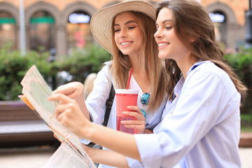 Wall Mural - Photo of two girls enjoying sightseeing outdoor. Beautiful female tourists exploring city with map.