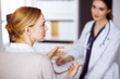 © rogerphoto - Cheerful smiling female doctor and patient woman discussing current health examination while sitting in sunny clinic. Medicine concept