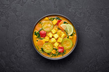 Yellow Veg Thai Curry With Tofu And Vegetables In Black Bowl At Dark Slate Background. Vegetarian Thai Curry With Tofu, Zucchini, Pepper, Spinach, Carrot. Thai Food. Indian Vegetable Curry. Copy Space