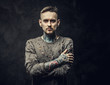 © Fxquadro - Inked young man wearing grey ripped jumper posing looking serious and calm, isolated on a grey background in a dark studio. Close up photo