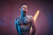 © Fxquadro - Self-assured male model posing in a neon studio with a half-naked body wearing fire-shaped sunglasses and tattooed in a japanese irezumi style, looking cool and relaxed.