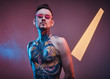 © Fxquadro - Self-assured male model posing in a neon studio with a half-naked body wearing fire-shaped sunglasses and tattooed in a japanese irezumi style, looking extravagant.