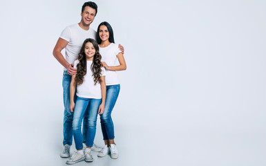 Wall Mural - Happy beautiful young family in white t-shirts while they hugging each other isolated on a light background.