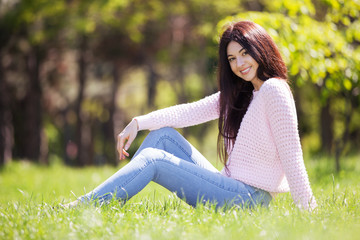 Wall Mural - Young woman relax in the park on green grass. Beauty nature scene with colorful background, trees at spring season. Outdoor lifestyle. Happy smiling woman sitting on green grass