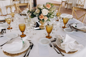 banquet tables are decorated with compositions of flowers and greenery, on the tables are plates with napkins, glasses, candles and name cards